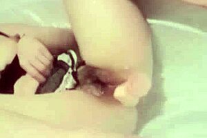 This Asian girl is masturbating in the bathroom with a dildo while watching porn.