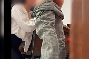 una maestra y su alumno en el salon de clases lo manda a llamar y los graban detras de la puerta